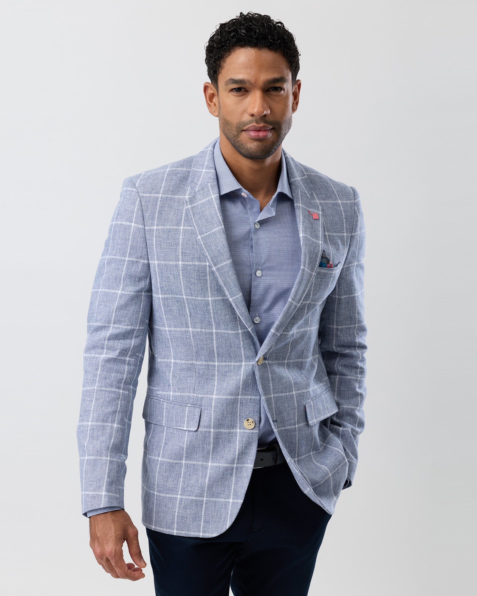 Man wearing a light blue checkered blazer over a light blue shirt on a white background